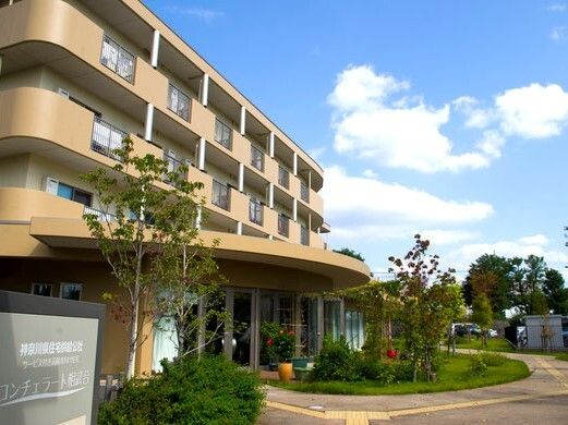 日当たりのいい場所に建っている４階建ての建物の玄関には屋根が付き、その周りには点字ブロックが敷かれている。