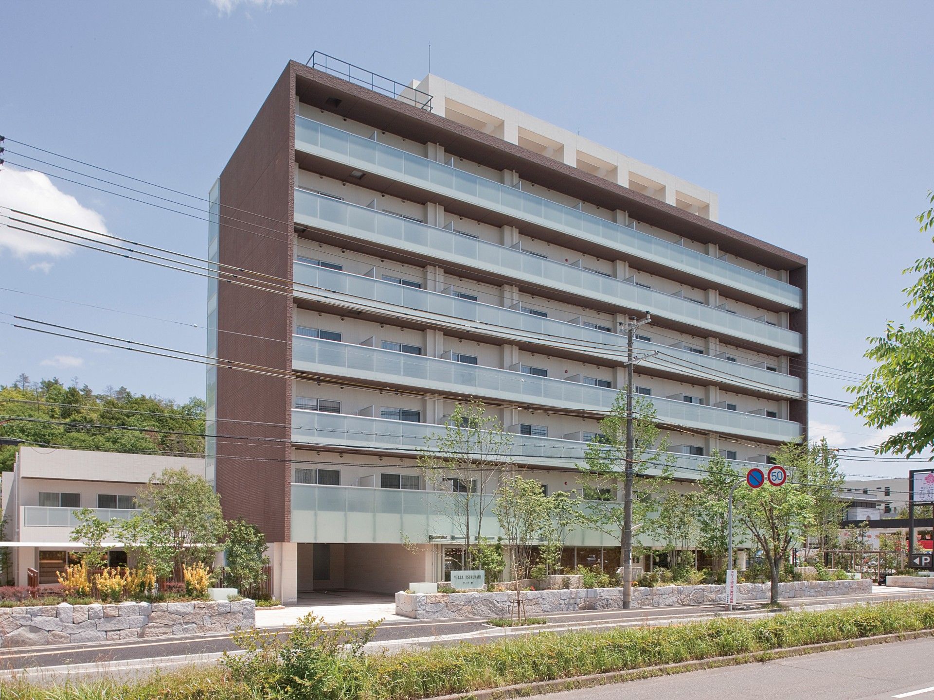 白色と茶色を基調とした外壁の、一部８階建ての施設である。片側２車線の幅の広い道路に面している建物。