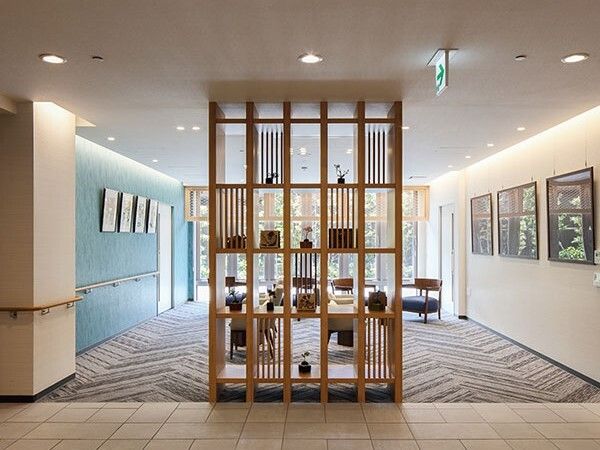 カーペット敷きの共有スペースにはたくさんの絵画が飾られている。廊下との間には棚が置かれ、仕切りの役割をしている。