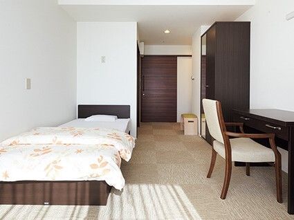 カーペットが敷かれた一人用の部屋にはデスクやいす、寝具付きのベッドが置かれ、クローゼットもある。
