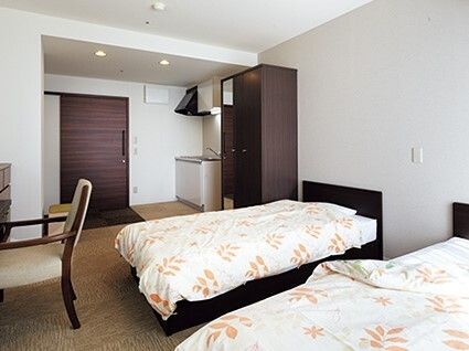 花柄の寝具がセットされたベッドが2台置かれた部屋にはキッチンもあり、デスクセットやクローゼットもある。