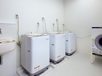 白い縦型の洗濯機が3台並んで設置された横には手洗いができる場所もあり、乾燥機もある。