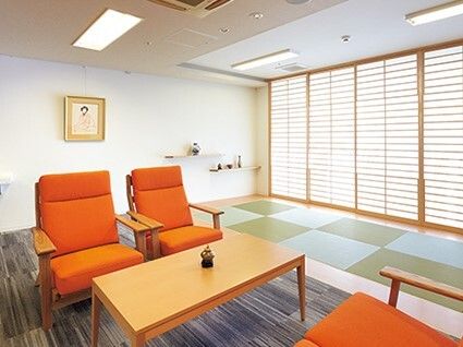 手前にはオレンジの椅子の応接セットがあり、奥には畳スペースがあり、窓には障子がセットされている。