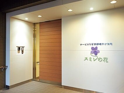 住宅名が書かれた白い壁には紫の菫の絵も描かれ、ライトが照らしている。ドアは重厚感のある木製のもの。