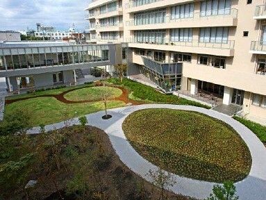 遊歩道が付いた庭園が左側にあり、右側にはベージュの建物があり、正面にはグレーの建物がある。
