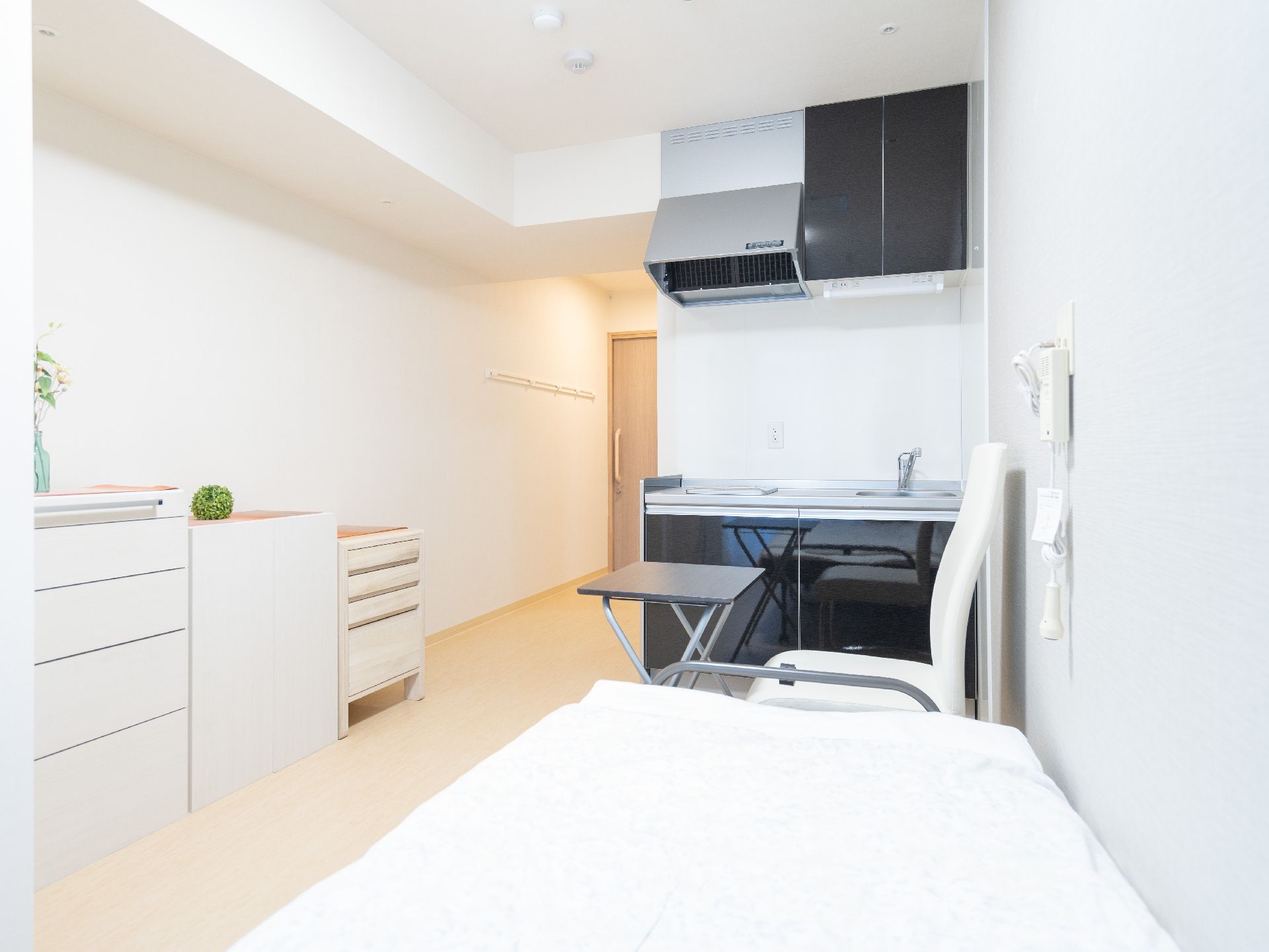 青い空の下に建っている3階建ての建物。ブラウン系で各フロアにベランダがあり、広い駐車場がある。