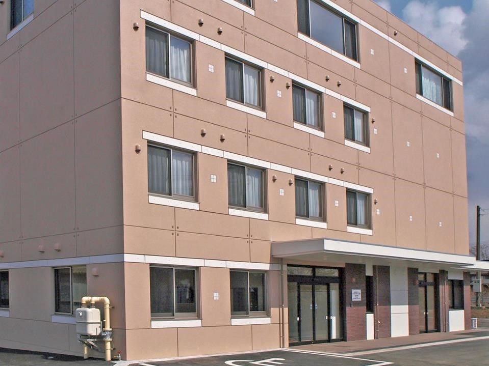 ４階建ての大きな建物で、玄関の上にはひさしがある。車椅子をご利用の方のために、玄関のすぐそばに専用駐車場をご用意している。