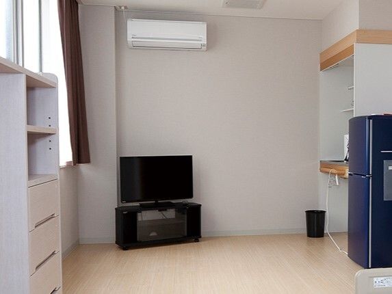エアコンやテレビ、収納家具、冷蔵庫が設置されたフローリングの部屋には車いす対応のキッチンもある。