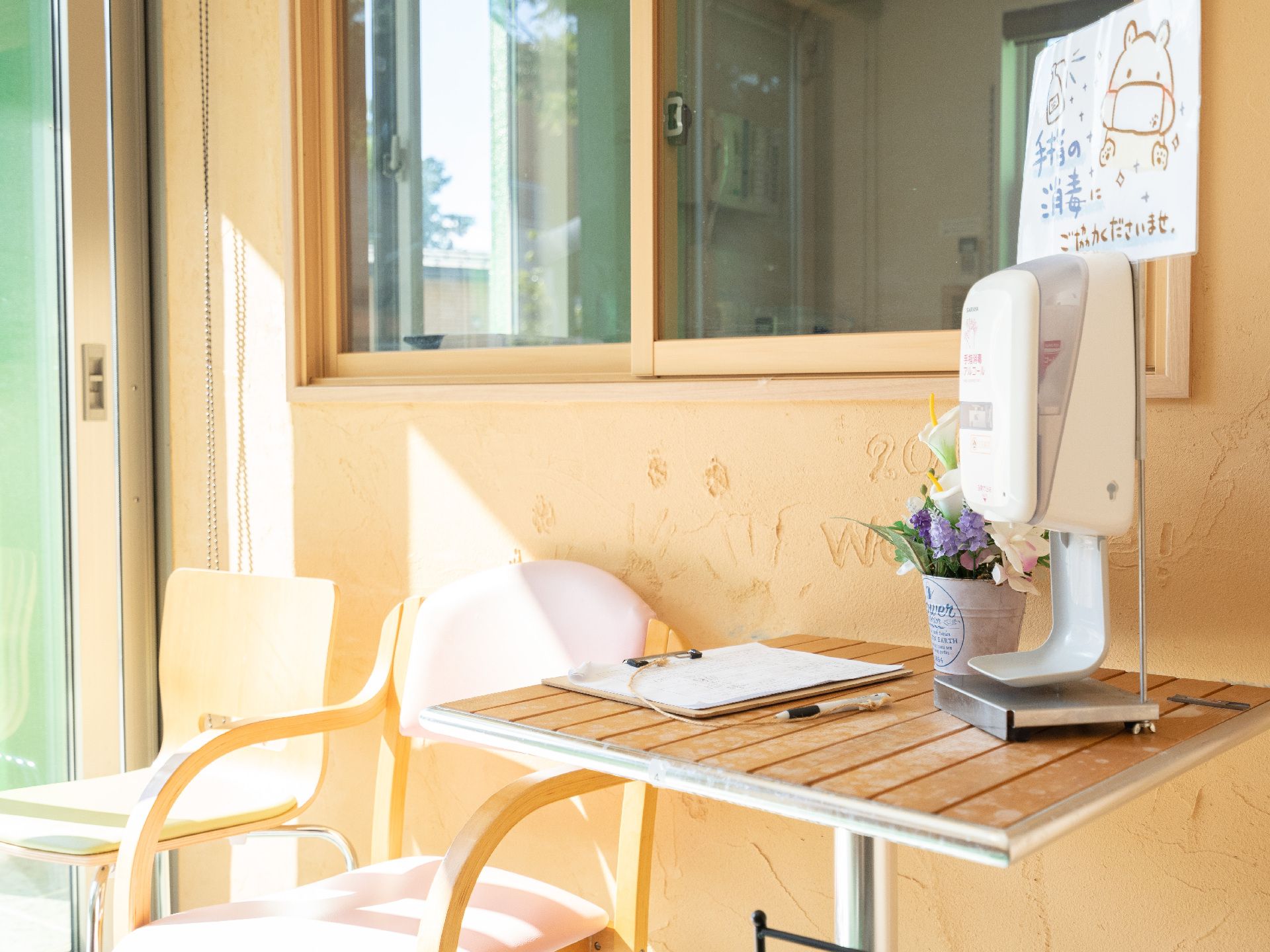原っぱのような場所を笑顔で散歩している高齢女性と付き添いの若い女性スタッフ。高齢女性はジャケットを羽織り、スタッフは半そでのポロシャツ姿。