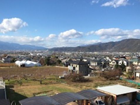 奥には山が連なり、手前には畑が広がり、中間には住宅がたくさん建っている。