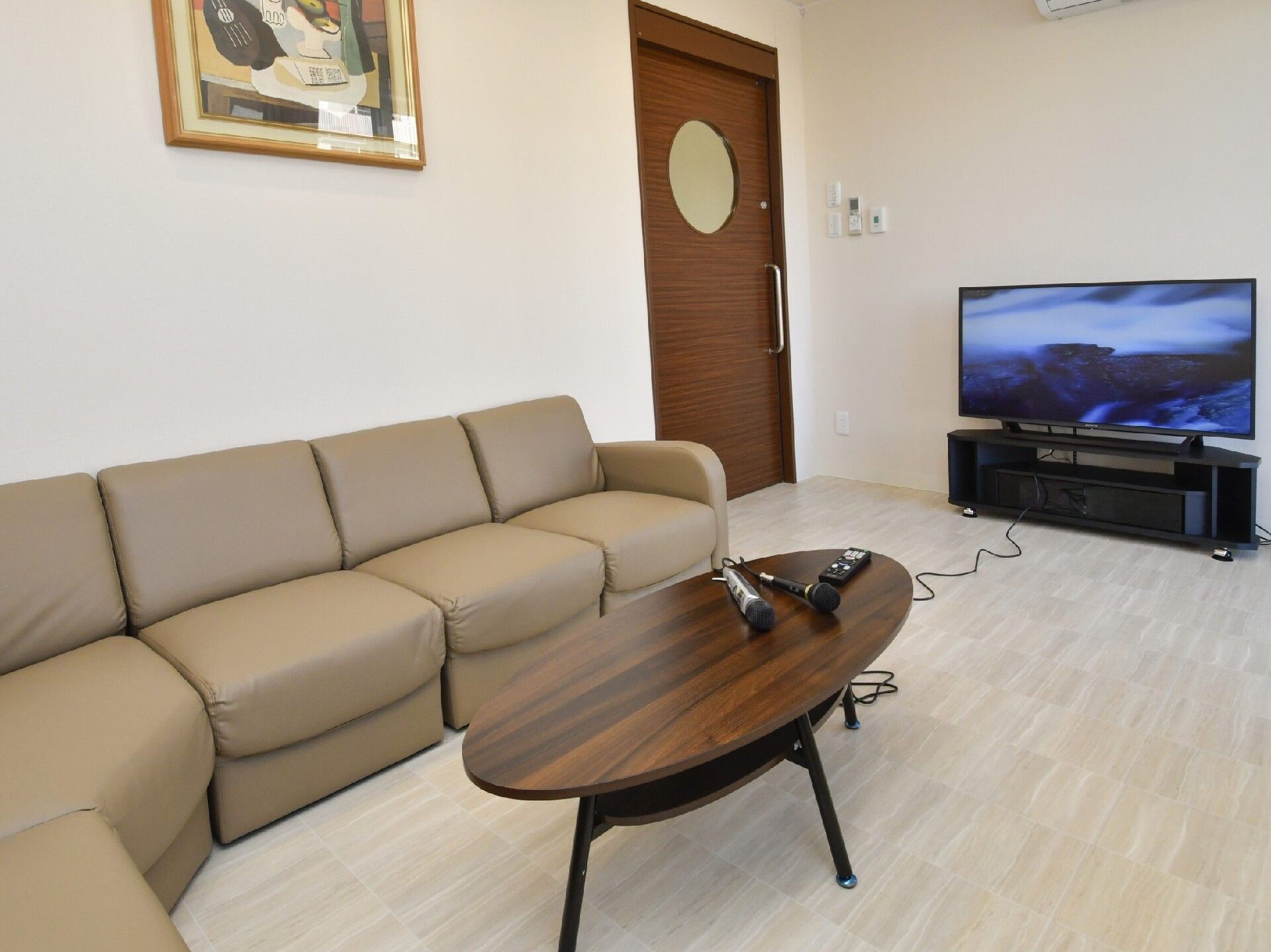 絵画が飾られたカラオケルームにはベージュのソファや大型テレビが設置され、テーブルの上にはマイクが置かれている。