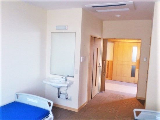 介護仕様のベッドと洗面台、奥のほうにトイレが置いてある個室仕様の部屋の様子