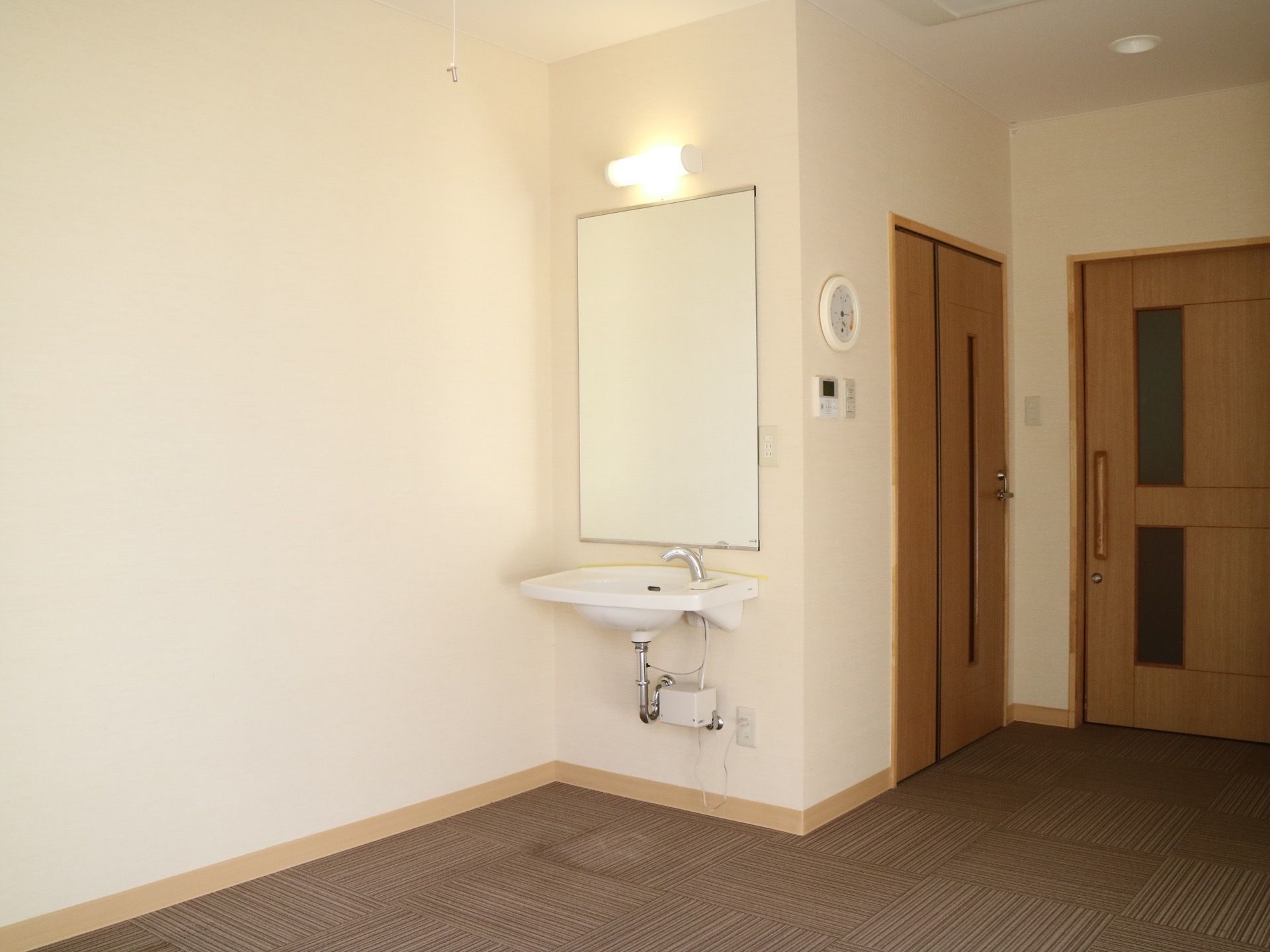 居室には洗面所があり、壁に照明と大きな鏡が設置されている。床は全面に茶色いカーペットが敷かれている。
