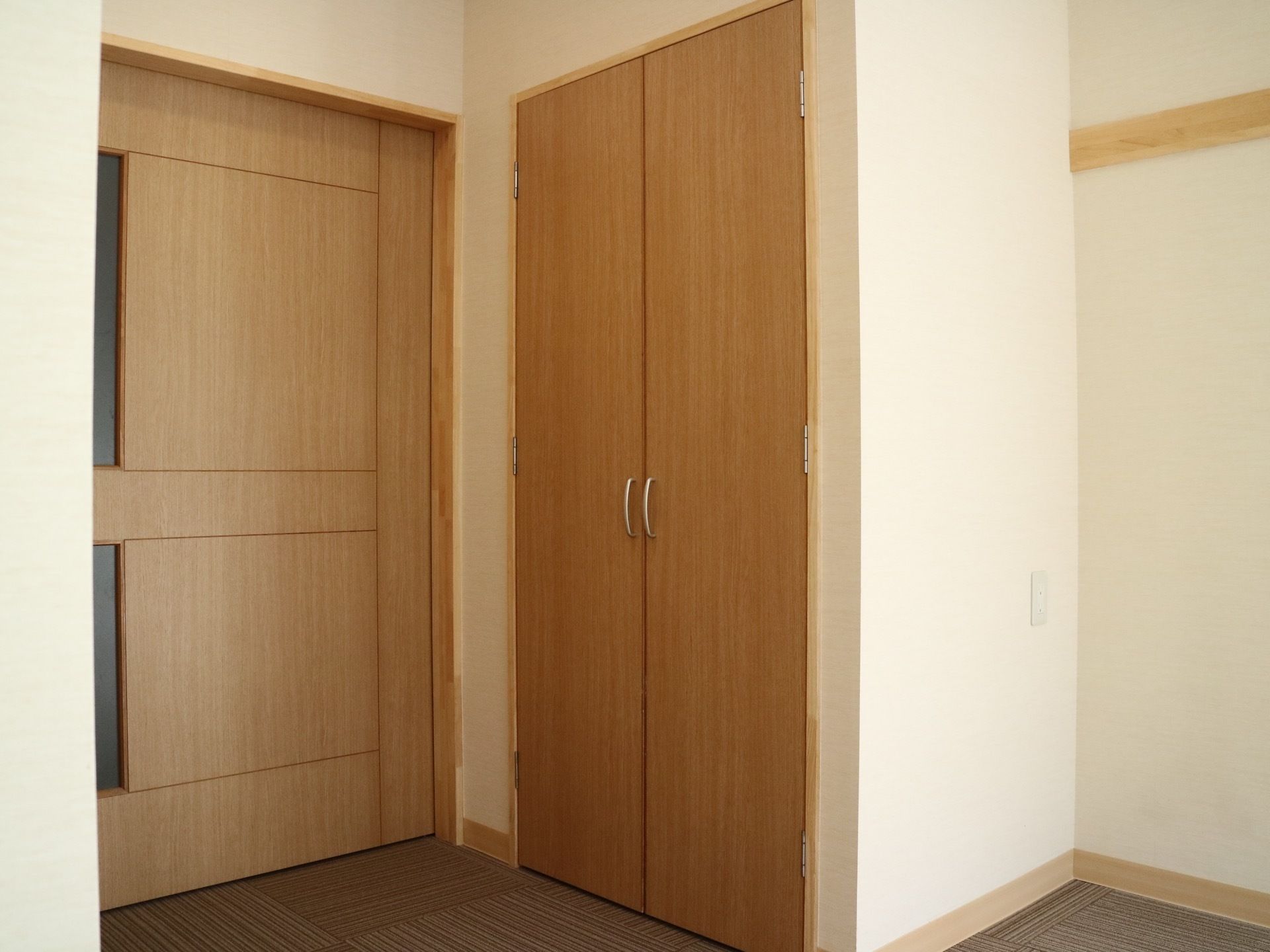 両開きの扉が付いたクローゼットが備えてある。その横には幅の広い引き戸があり、壁にはコンセントパネルが設置されている。