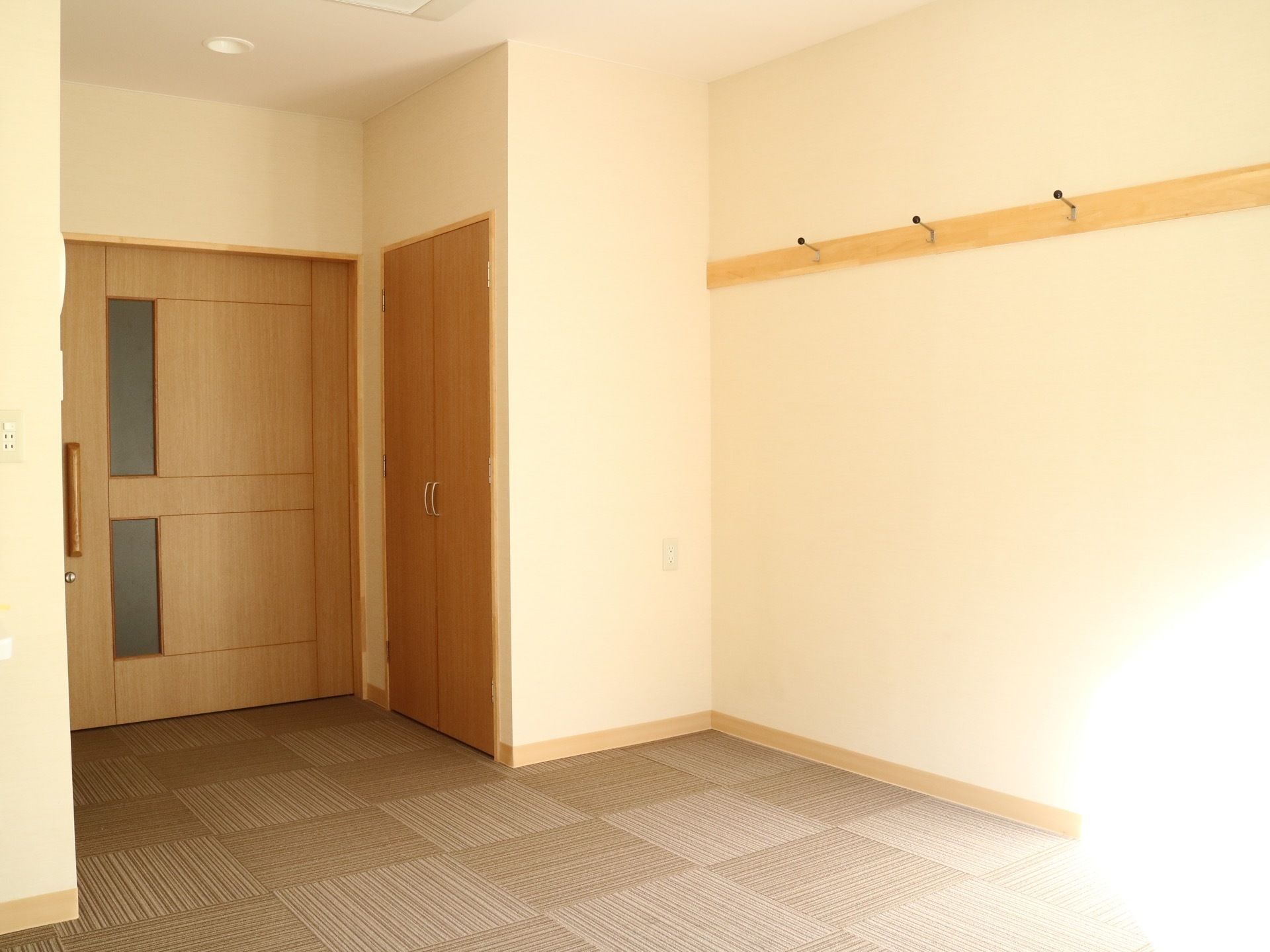 居室の壁にはコンセントパネルと洋服掛けが設置されている。室内は窓から入ってきた陽の光により明るくなっている。