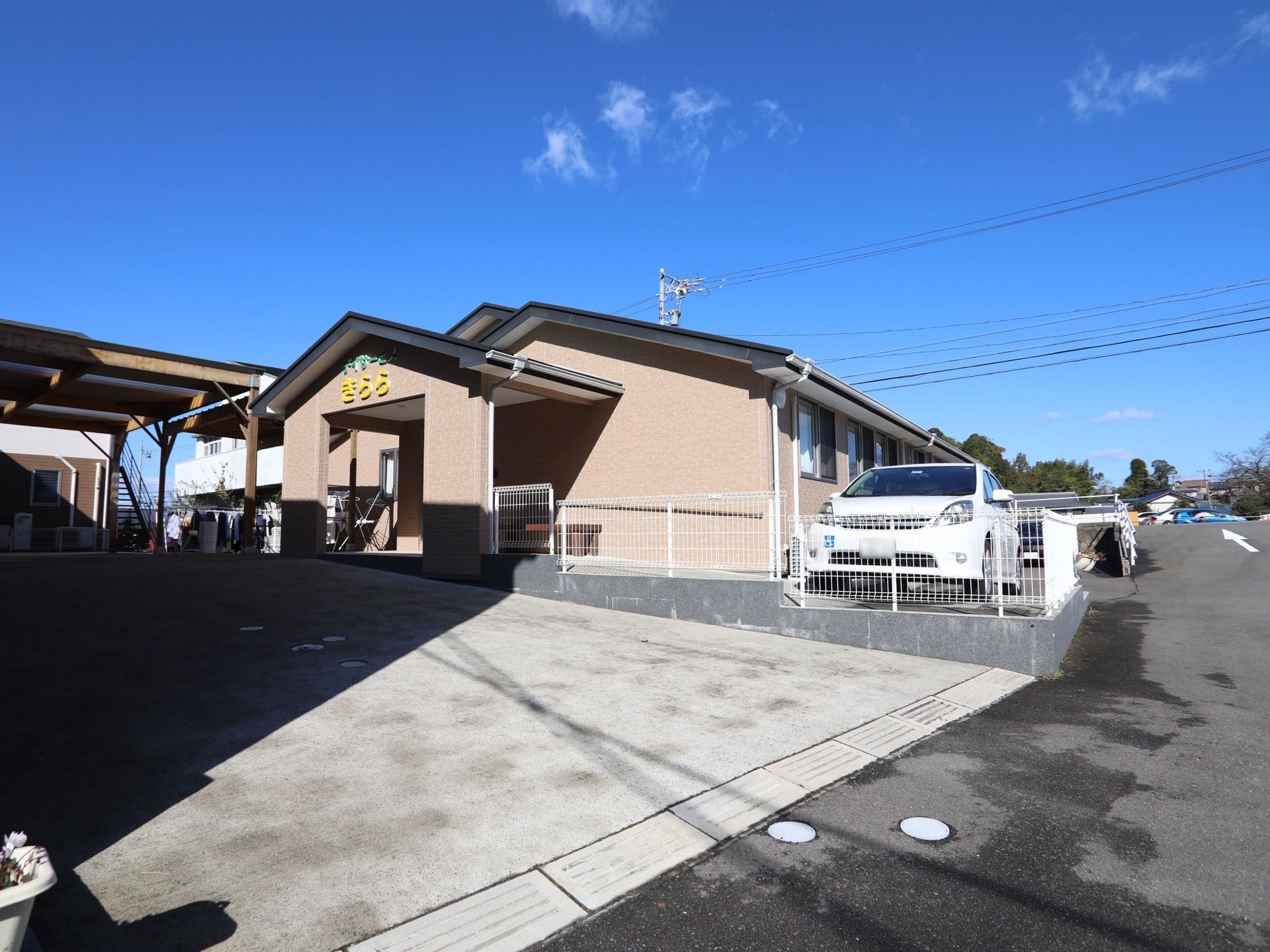 隣接した１階建てのグループホームである。玄関前に大きなひさしがあり、施設名が黄色の文字で示されている。