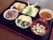 天ぷらの盛り合わせや赤飯、汁物、煮物、あえ物などが並んでいる黒いトレー。
