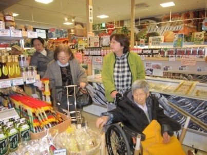 スーパーで買い物をする入居者とスタッフ。歩行器や車いすを使用する人もいる。