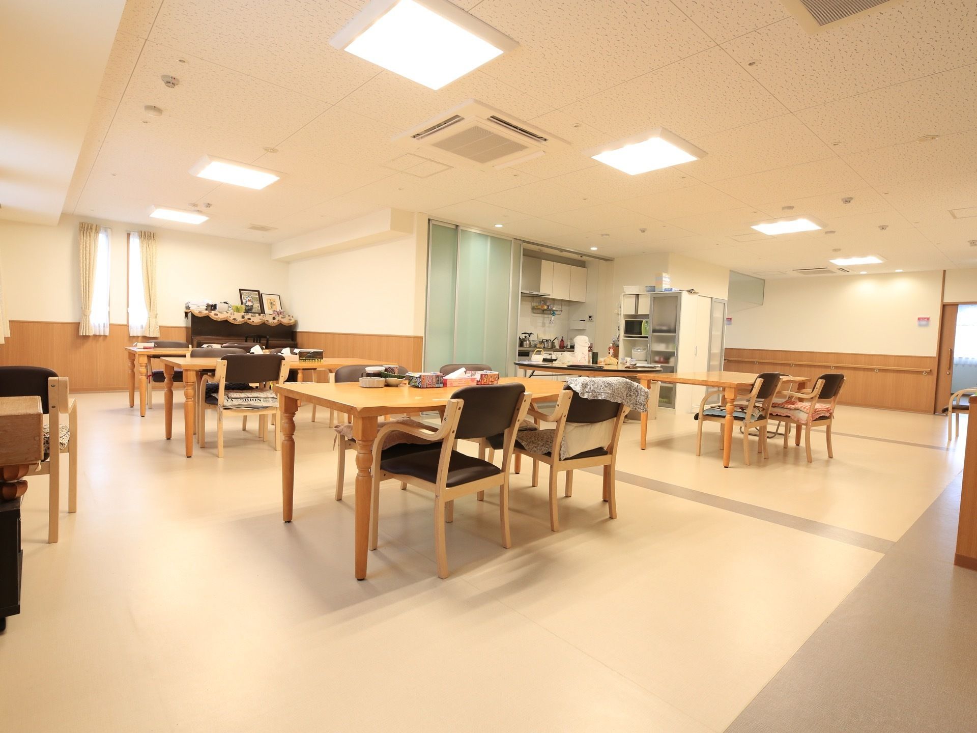 天井にエアコンと四角い照明が並んでいる。木製の長方形のテーブルに座面が濃い茶色の椅子がセットされている。