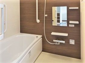 家庭的なサイズの浴室の様子。シャワーや大きめの浴槽がある落ち着いた色合いの浴室
