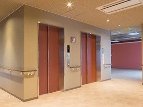 手すりが取り付けられている廊下とやわらかい照明があるエレベーターホール。ホテルのようなラグジュアリー感