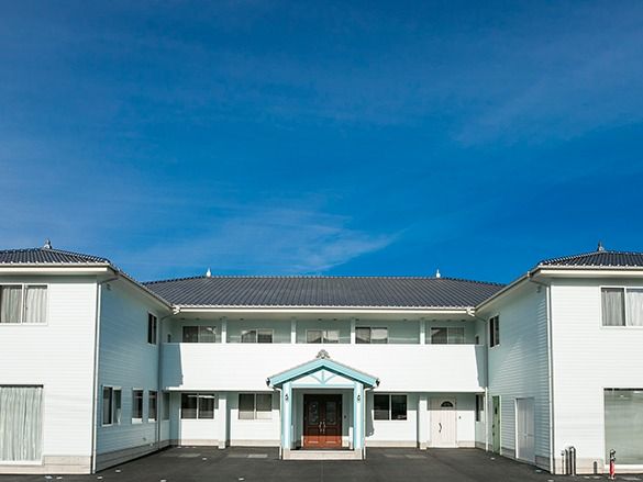 2階建ての建物はコの字型でグレーの屋根が付き、玄関部分には茶色のドアが付いている。