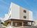 3階建ての建物。ベージュと白でまとめられ、周辺を住宅に囲まれた温かい雰囲気の外観。