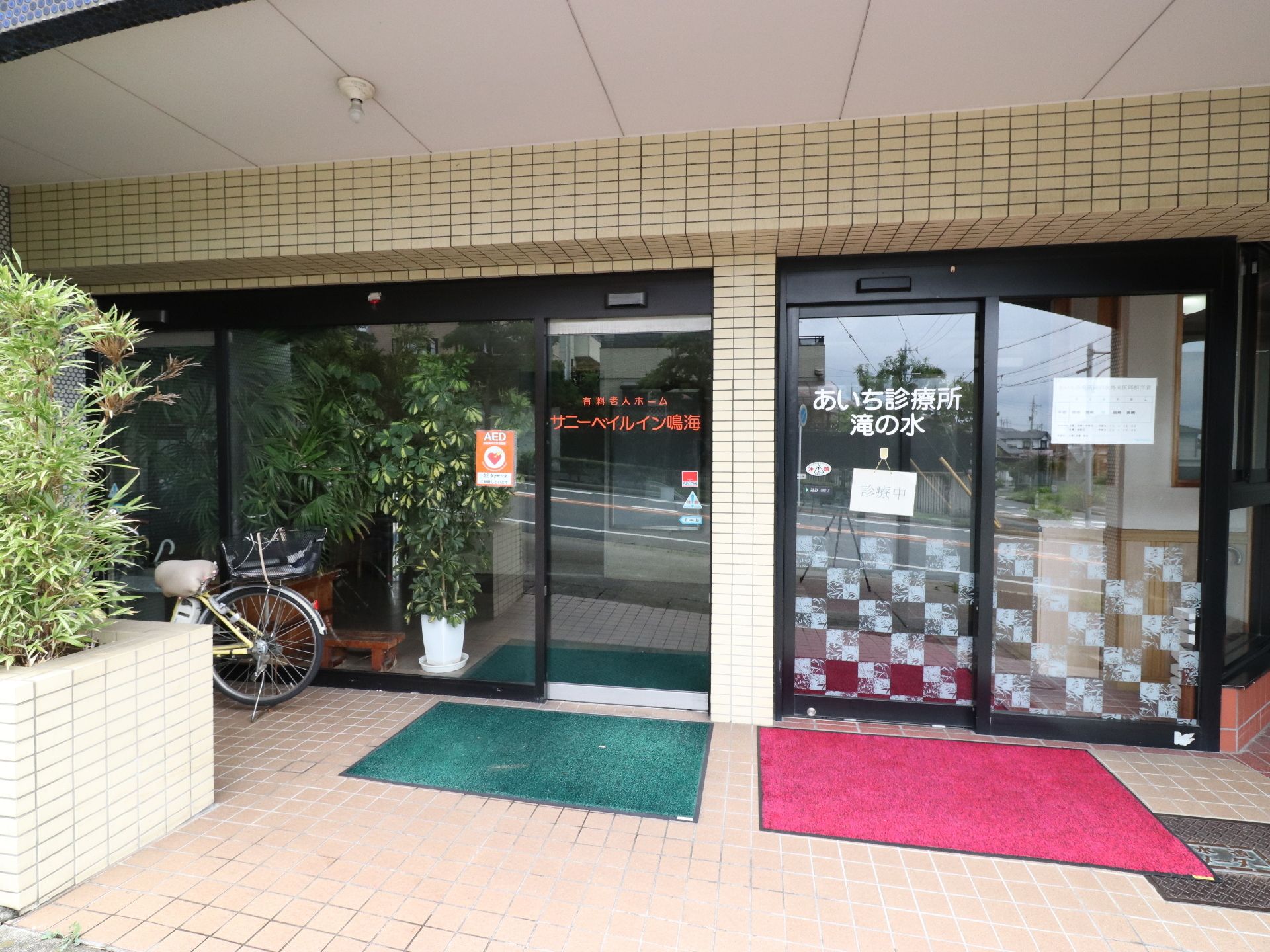 ベージュのタイル張りになっている施設の入り口には木が植えられ、ガラスの自動ドアへのアプローチはバリアフリー仕様。