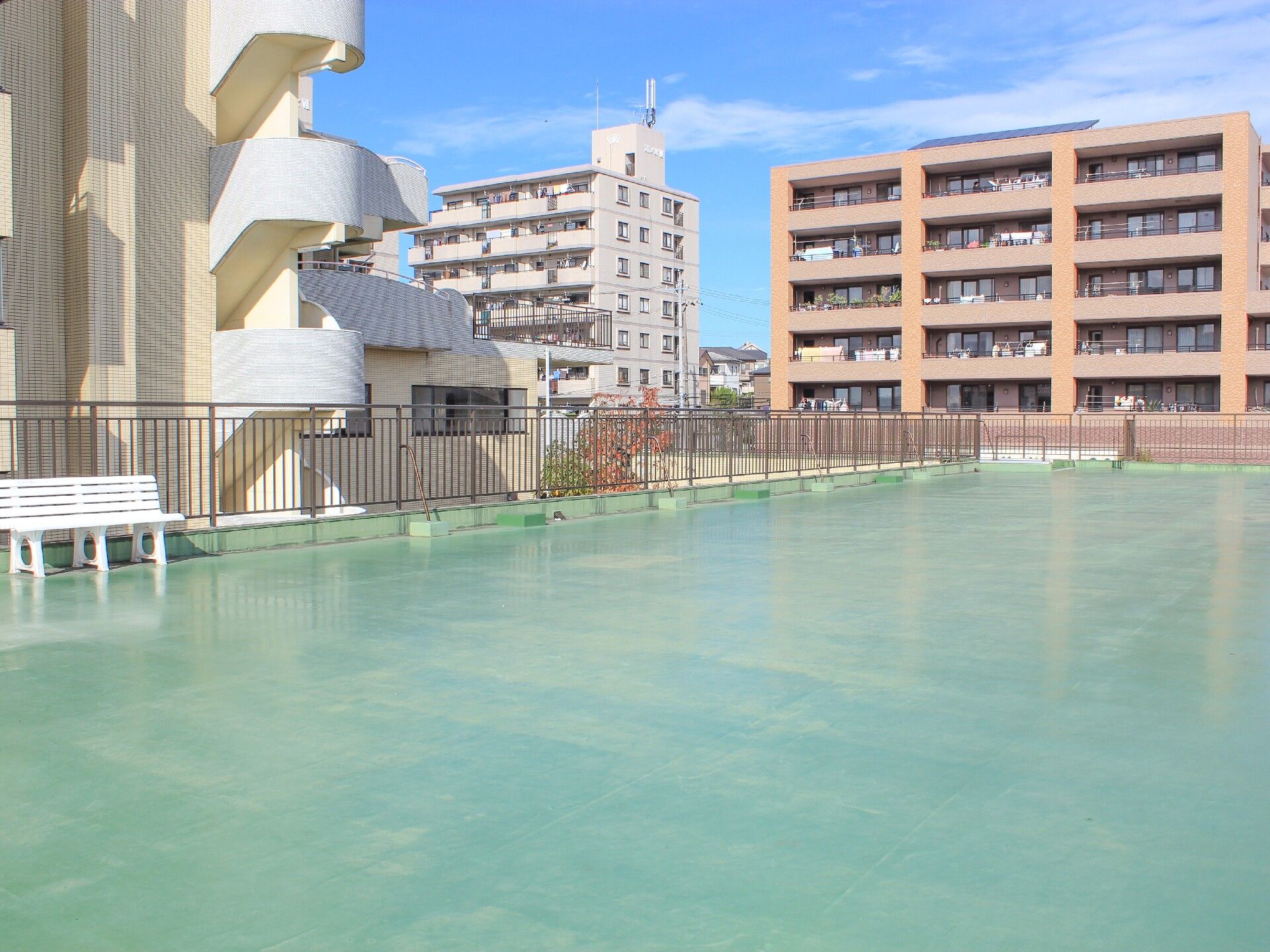 屋上には緑の床が広がっている。白い柵の上には薄いピンク色の手すりが設置されていて、安全対策がされている。
