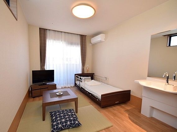 エアコンが付いたフローリングの部屋にはテレビや寝具付きのベッド、畳風のマット、ちゃぶ台などがあり、車いす対応の洗面所もある。