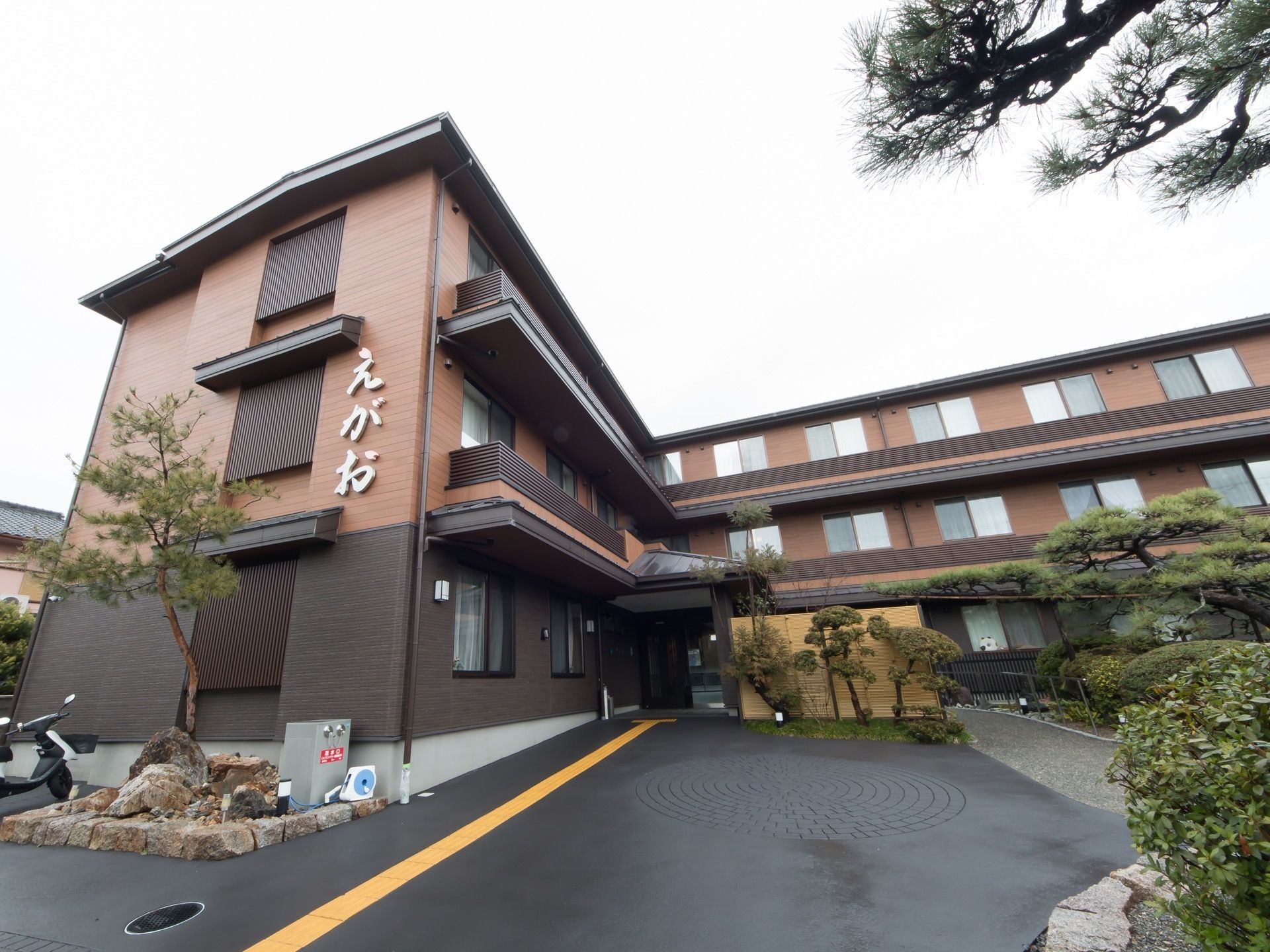 施設は３階建てで、外壁が茶色や黒で塗られている。施設周囲はたくさんの植物が植えられ、きれいに剪定されている。