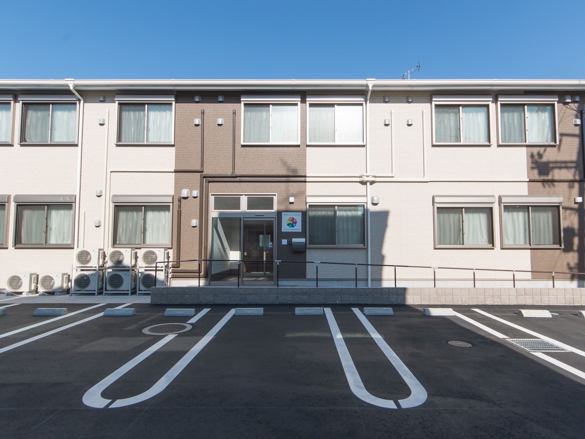 ベージュとブラウンの二色を基調とした、落ち着いた雰囲気の建物である。入口には施設のマークがあり、遠くからでも分かりやすい。
