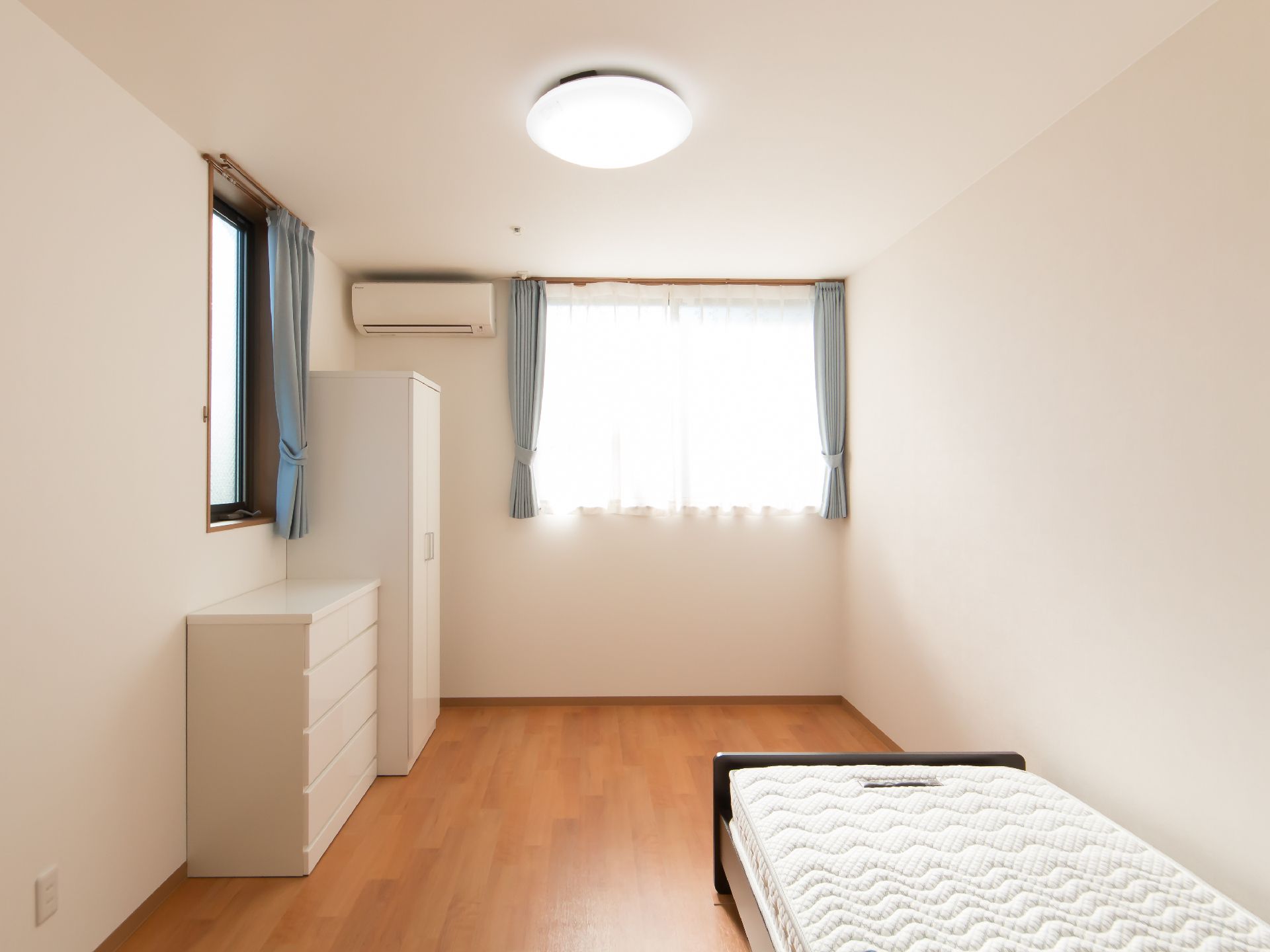 2つの白い収納家具とベッドが置かれている、複数の窓がある部屋