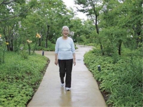 手入れされた新緑の間の遊歩道をこちらに向かって歩いてこられる高齢の女性
