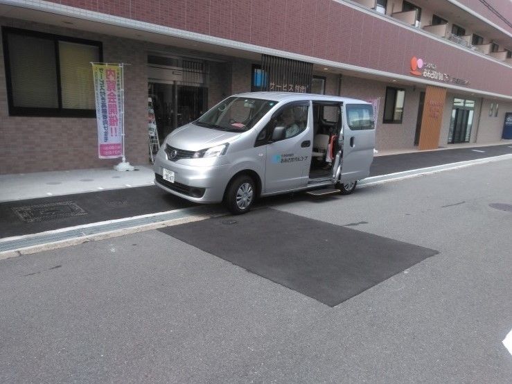 施設の前に停車しており、後部座席のドアが開いている銀色の送迎車