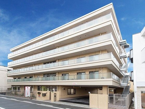 各フロアにベランダがあり、ベージュの外壁の５階建ての建物。道路に面して建っていて、館銘板がある。