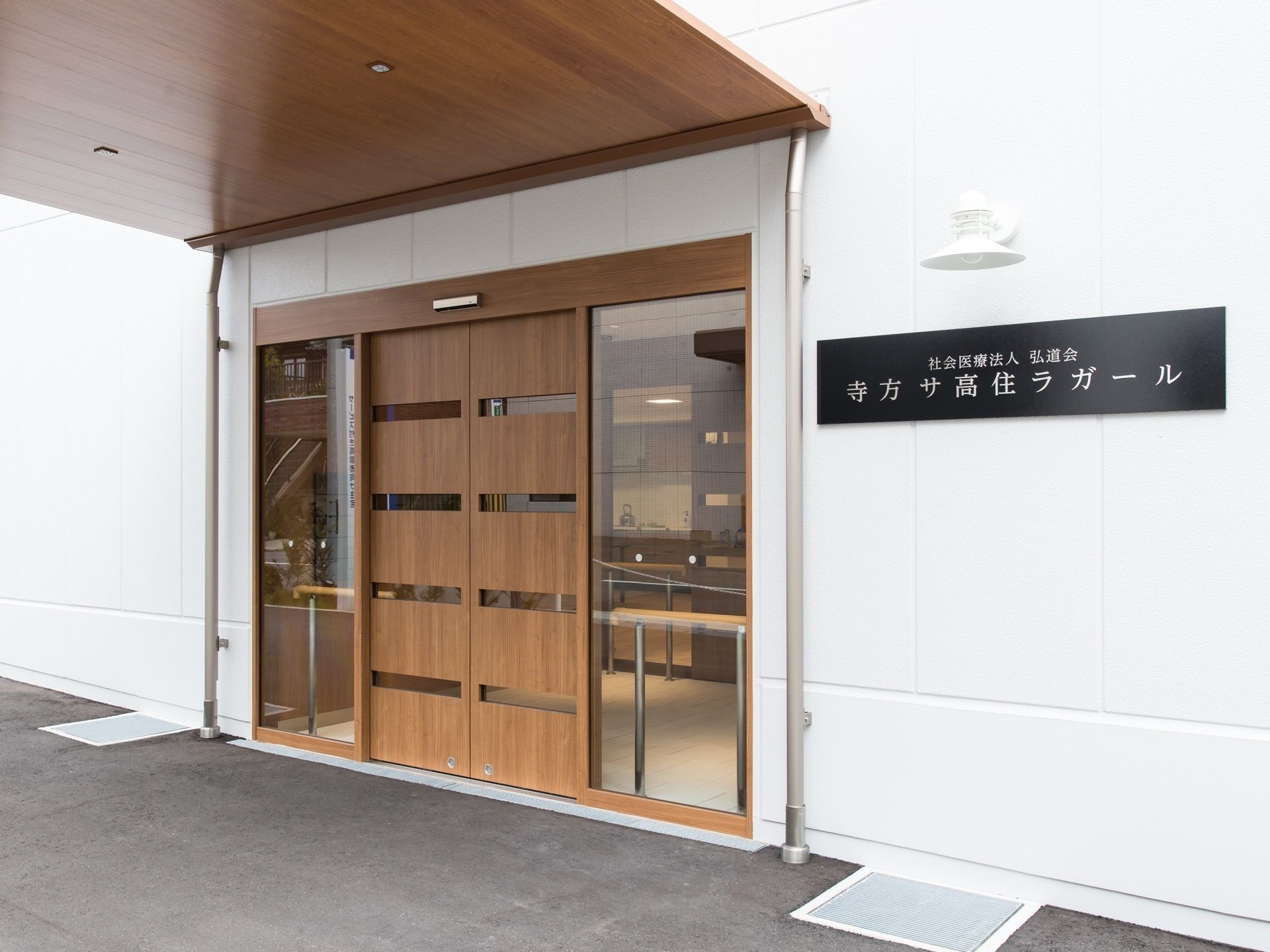 長方形の黒いプレートに、白い文字で施設名称が印字されている。その上には外壁ライトがあり、おしゃれな雰囲気である。