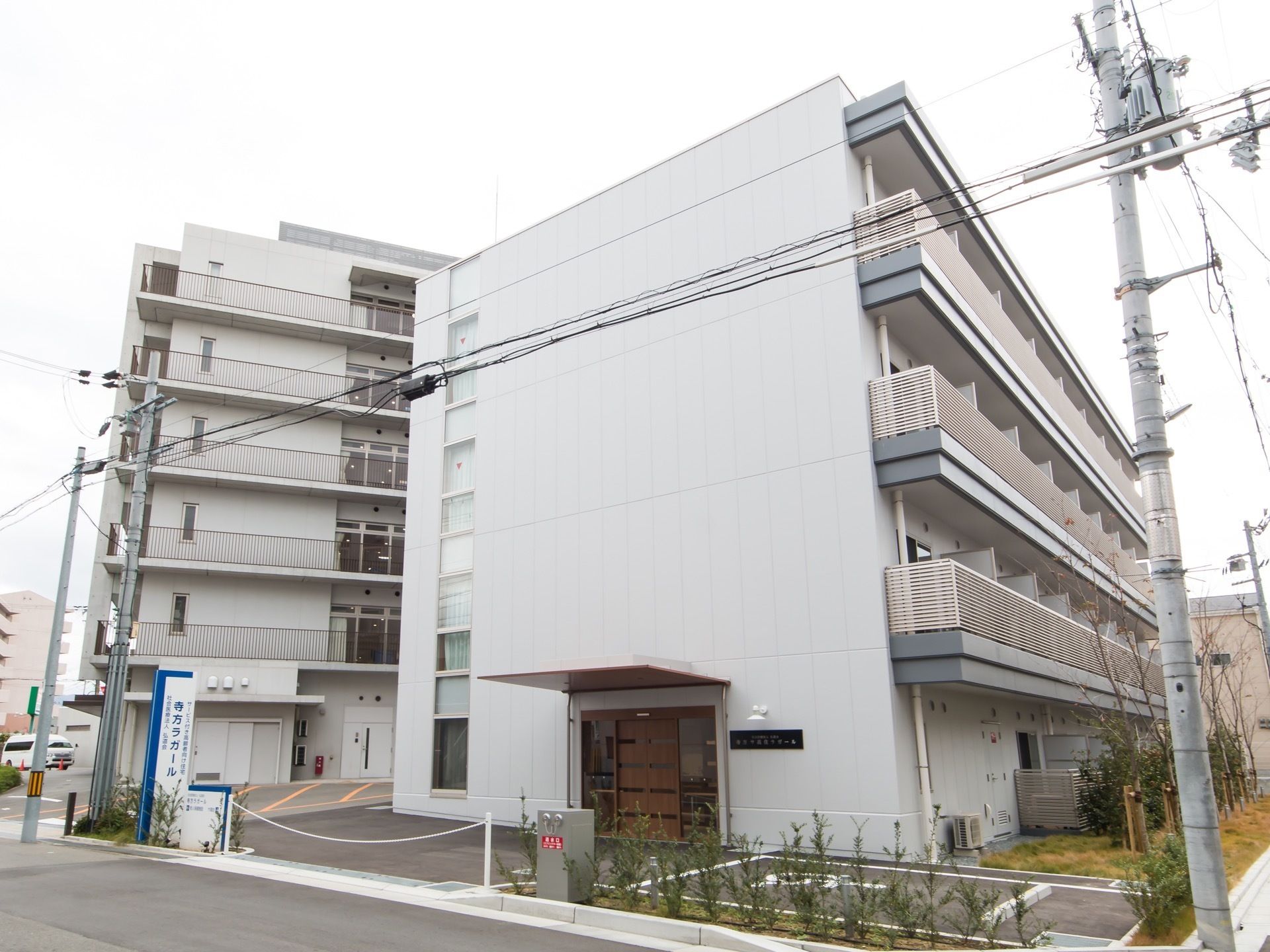 建物の右横と道路沿いに植え込みがあり、数種類の草木が生えている。玄関のすぐ近くには、身障者用の駐車場がある。