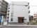 全体的に白でまとめられたシンプルなデザインの建物である。左端には看板があり、青い文字で施設名が書かれている。