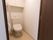 木目調のドアで仕切られたトイレがある。背面には棚が備え付けられており、便座横の壁にはL字型の手すりがある。