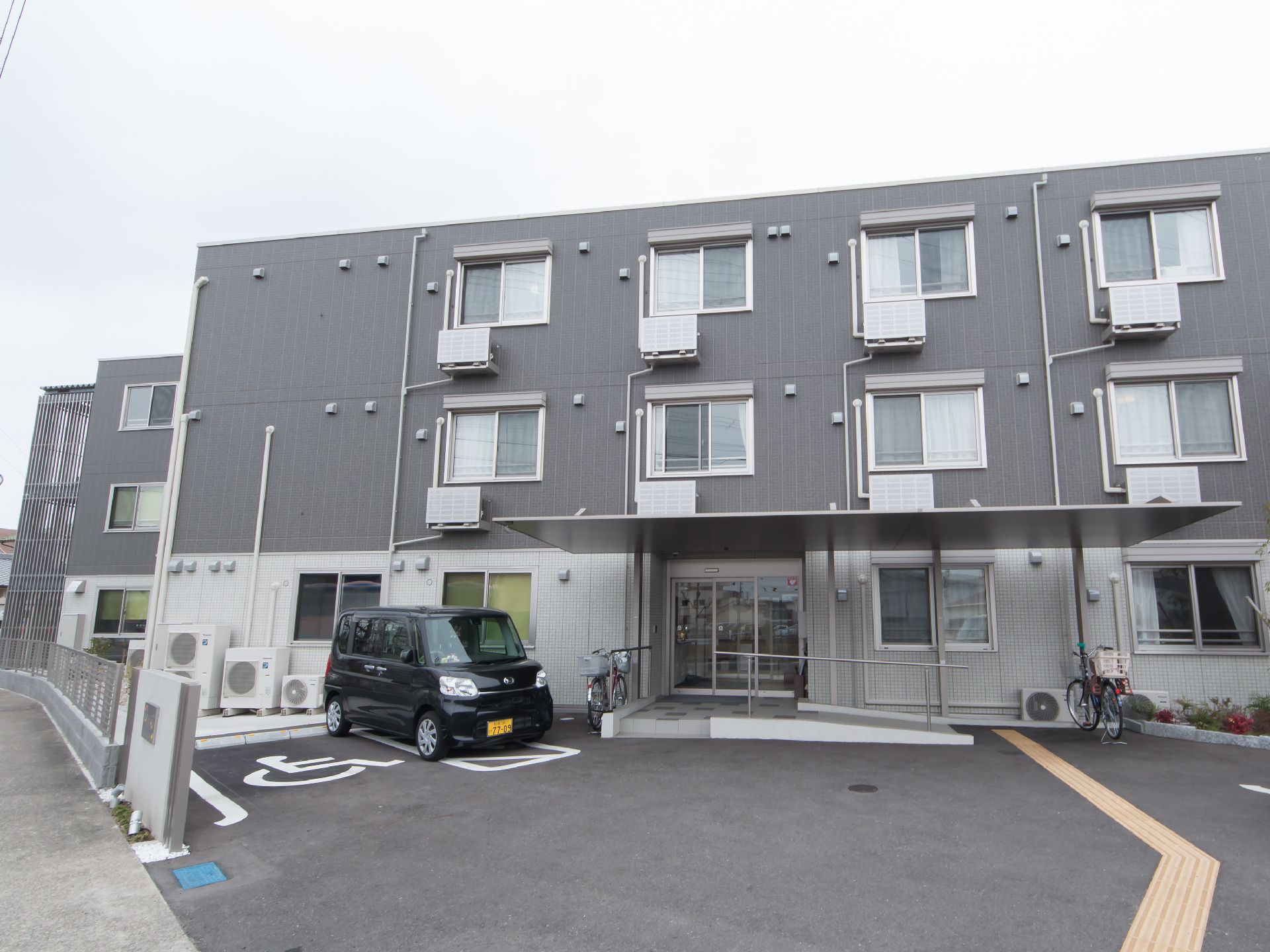 モノトーンの外壁が施された3階建ての建物と舗装された駐車場