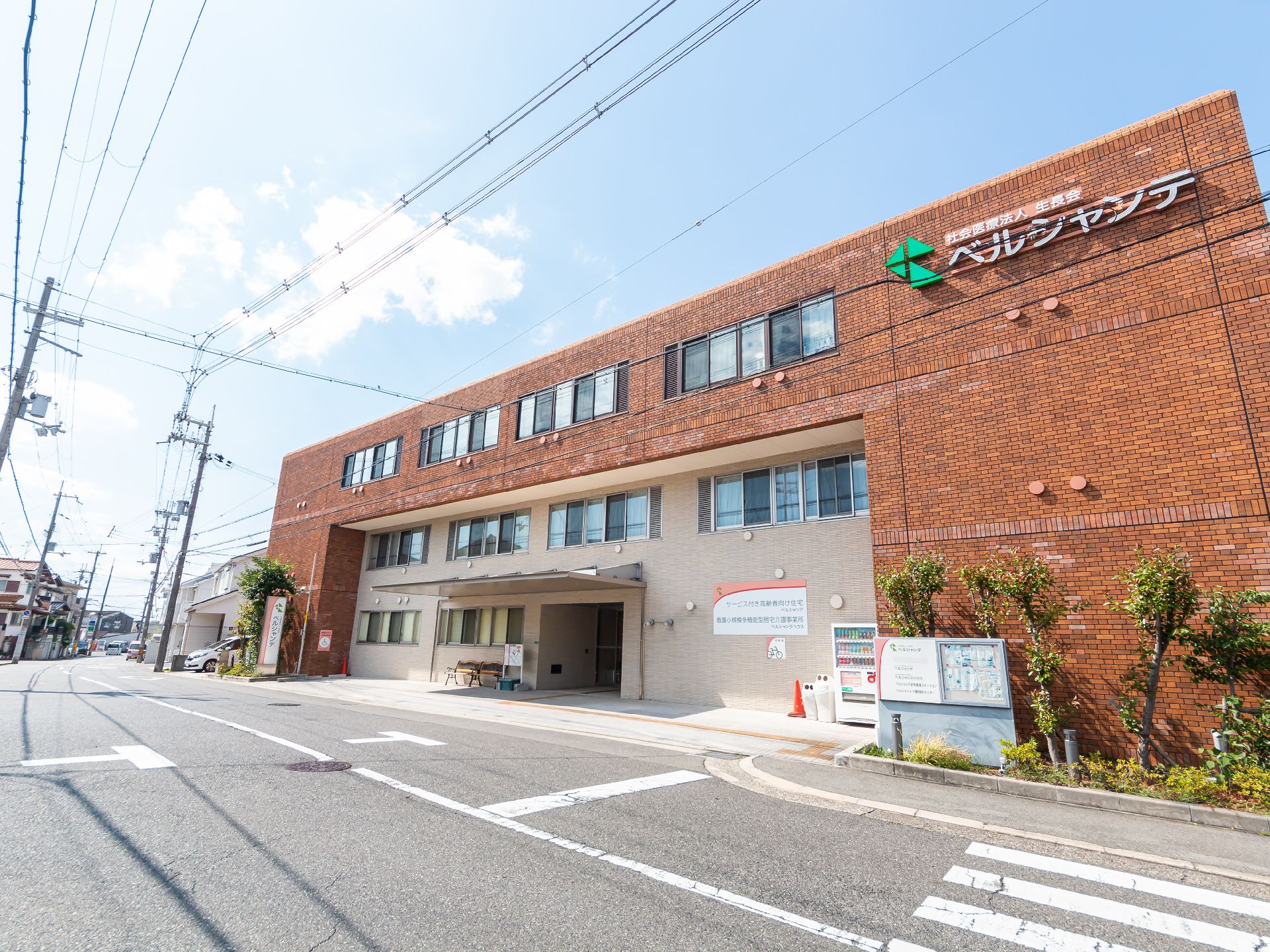 高齢者2名とスタッフが手を握りながら談笑している様子。施設内の会話の一画面