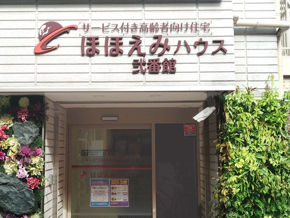 白髪の高齢女性とピンクのポロシャツ姿の女性スタッフが手をたたきながら笑っている様子。
