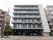 ６階建てのマンションのような建物で、２階以上の部分にはベランダスペースが設けられている。玄関前には、車が数台停められている。