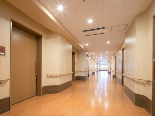 手すりが全域に付いた明るい雰囲気の廊下。まっすぐで両サイドに居室のドアがある。
