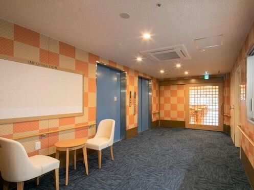 エレベーターが設置されたフロアの一角。手すりが壁につき、ホワイトボードの前には二人用のテーブルセットもある。