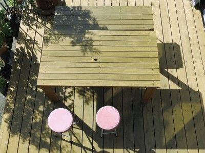 自然な色のウッドテラスには大きな四角いテーブルと丸椅子が２脚置かれている。