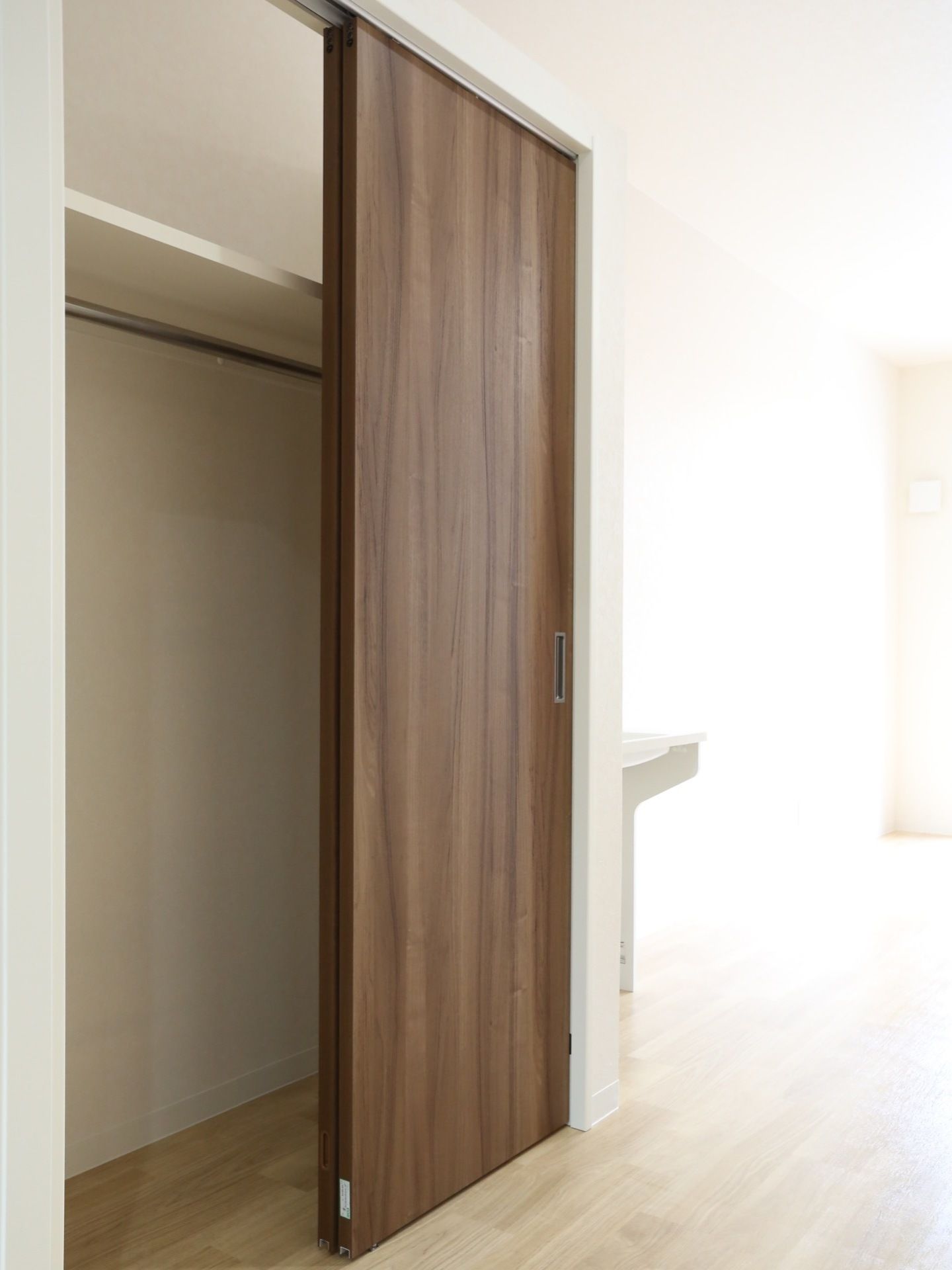 ダークブラウンの木目調のドアの奥に収納スペースがある。ハンガーを使って衣服をかけることができるポールが設置されている。