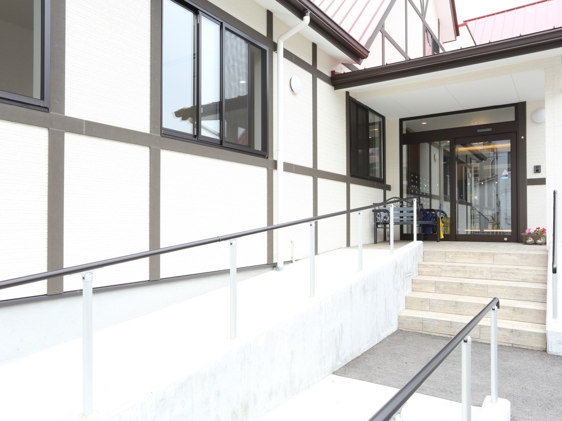 玄関前には階段があり、階段の横にスロープが設置されている。玄関のドアは自動ドアであり、ドアの横にベンチが置かれている。