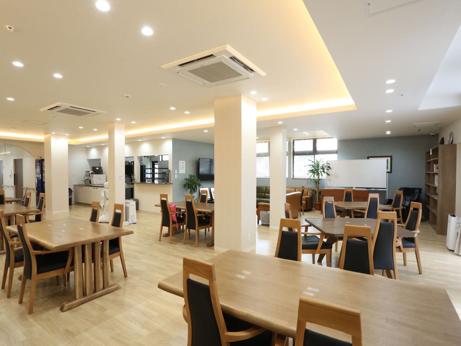 広々とした共有スペースに、落ち着いた色合いのダイニングテーブルと椅子がいくつも置かれている。ホワイトボードやテレビがある。